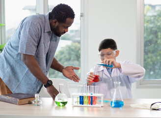 Teacher and child student studying chemical science in classroom. Multiracial male tutor teaching liquid experiment to boy pupil in class. Schoolboy back to school and learning with multiethnic person