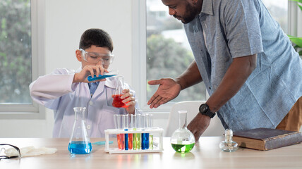 Teacher and child student studying chemical science in classroom. Multiracial male tutor teaching liquid experiment to boy pupil in class. Schoolboy back to school and learning with multiethnic person