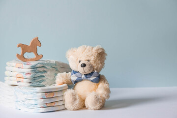 Wooden toys, a bear in a bow tie, a stack of diapers and baby supplies on the changing table. Space for text.
