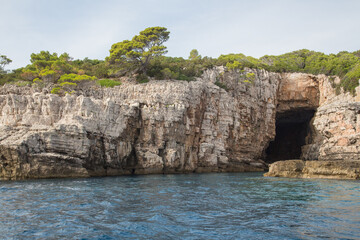 Fototapeta na wymiar Landscape with pinewoods above limestone walls, scarps and a blue cave on Lokrum island in the Adriatic Sea with its beautiful turquoise water near Dubrovnik, Croatia