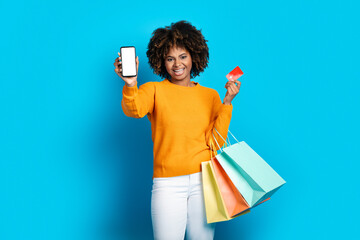 Excited lady with shopping bags showing phone and credit card
