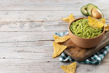 Mexican guacamole with nacho chip in wooden bowl on rustic wooden table. Copy space. Traditional...