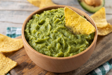 Mexican guacamole with nacho chip in wooden bowl on rustic wooden table. Traditional mexican food