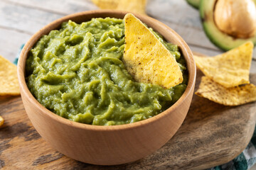 Mexican guacamole with nacho chip in wooden bowl on rustic wooden table. Traditional mexican food