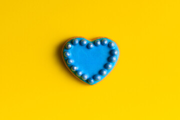 Cookie in shape of heart decorated by blue icing and sprinkles against yellow background