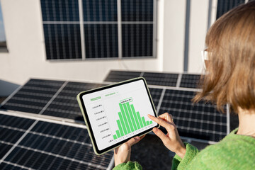 Woman monitors energy production from the solar power plant with a digital tablet. View on tablet...