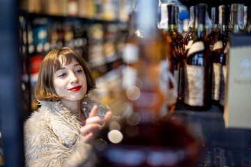 Woman chooses strong alcohol standing between rows of bottles in a supermarket. Buying cognac drink in alcohol shop