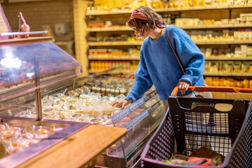 Young woman buying cheese, standing with shopping trolley in supermarket. Concept of shopping dairy...