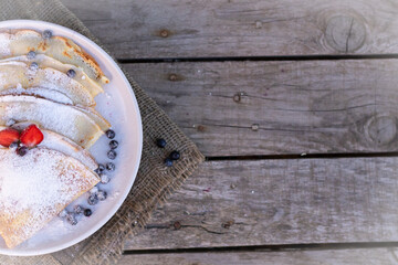Pancakes with blueberries and mint leaf on top. A bunch of big homemade pancakes with forest fruits. A pile of flat thin cake in the background on a white plate.,wooden background with copy space