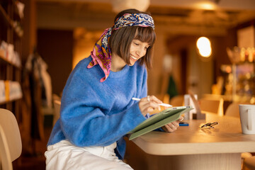 Young adult woman works on a digital tablet while sitting at modern coffee shop. Concept of remote creative work online