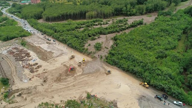 Aerial of an excavator and wheeled bulldozers removing massive mudflow from the roadway. Natural disaster.
