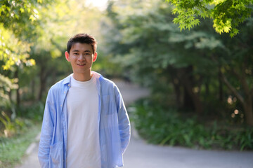 portrait of handsome Chinese young man smile at camera, with green trees under sunshine