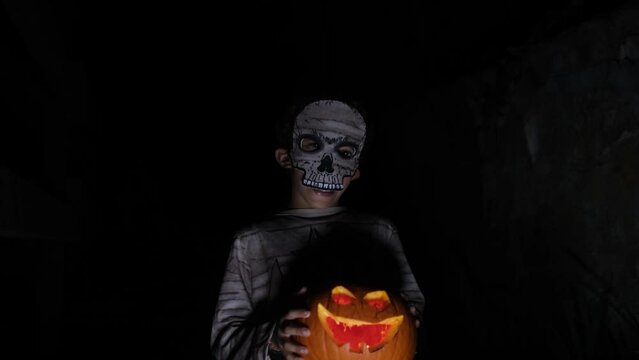Boy dressed as mummy with illuminated halloween pumpkin with bela at night terror trick or treat hallowen autumn celebration