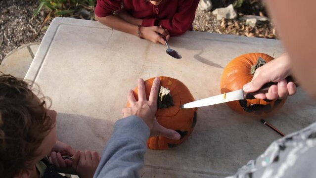 Preparing pumpkin for Halloween. Mother with children drawing out details of the face of the carved Halloween pumpkin. Emptying seeds inside pumpkin outlining the face eyes mouth with knife 