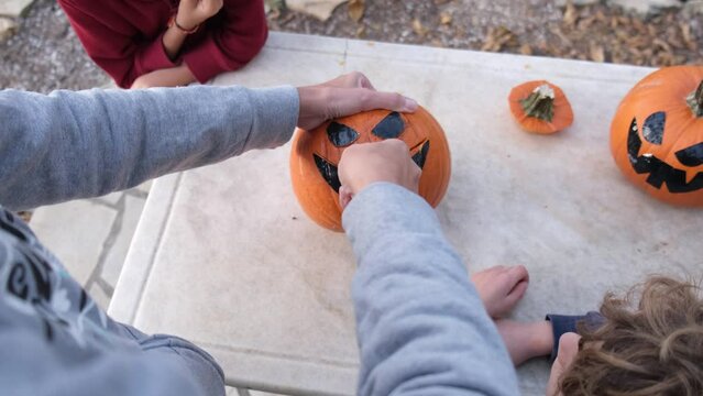Preparing pumpkin for Halloween. Mother with children drawing out details of the face of the carved Halloween pumpkin. Emptying seeds inside pumpkin outlining the face eyes mouth with knife 