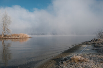 Autumn morning landscape. Sunrise over the lake in fog. The beginning of winter, the roe on the trees and grass.