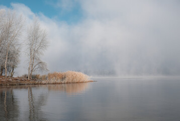 Autumn morning landscape. Sunrise over the lake in fog. The beginning of winter, the roe on the trees and grass.