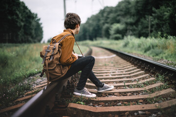 Photographer in brown jacket with backpack and retro camera on railroad