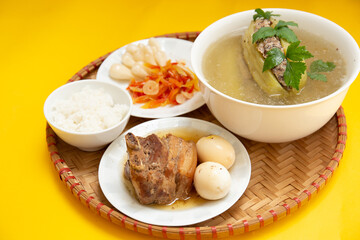Family dinning table of Tet holiday or Lunar New Year with traditional foods: pork belly and eggs braised in coconut water, pickles, rice, Banh Tet (rice cake), fried vegetables, bitter melon soup