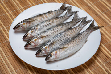 Five silver mullets lie on a white plate, on a bamboo rug