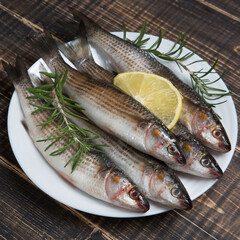 Five peeled fresh mullet fish lies on a white plate, a slice of lemon and rosemary on top