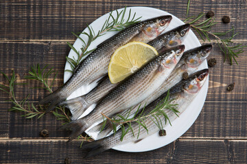 Several peeled fresh mullet fish lie on a white plate, topped with a slice of lemon and rosemary