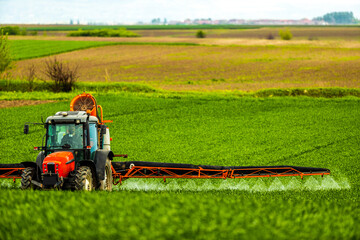 Wheat field protection with tractor-applied herbicides, pesticides, and fungicides, farmer ensuring...