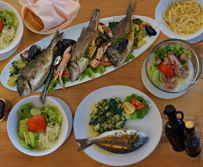 Appetizing seafood as lunch .Langoustines , red mullet, sea bass grilled with lemon, potato  ,shellfish ,pasta ,bread, sauce and salad on the table in the restaurant , Croatia - 565902300