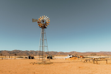 Abandoned derelict old car graveyard and old rusty wind turbine in the sandy desert with a blue sky on the background