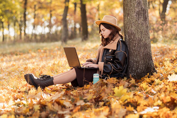 Woman sitting on foliage at park working on laptop. Girl using laptop while sitting under a tree at...