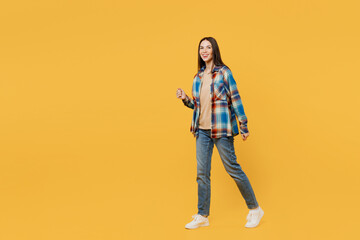 Full body side view young smiling cheerful caucasian woman wears blue shirt beige t-shirt walk go strolling look camera isolated on plain yellow background studio portrait. People lifestyle concept.