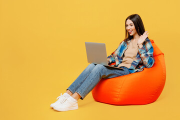 Full body young fun IT woman wear blue shirt beige t-shirt sit in bag chair hold use work on laptop...