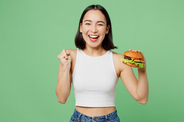 Young fun excited woman wear white clothes hold eat burger do winner gesture clench fist isolated...
