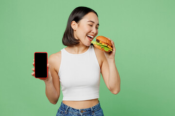 Young woman wear white clothes hold eat biting burger use mobile cell phone blank screen isolated...