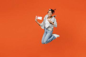 Fototapeta na wymiar Full body surprised young woman of African American ethnicity in grey shirt headband jump high hold point finger on gift certificate coupon voucher card for store isolated on plain orange background