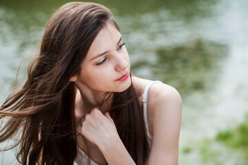 Fototapeta premium Young beautiful brunette girl in posing against the background of a pond in a summer park