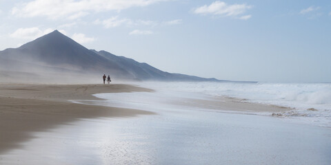 Beach view with waves, fog and sea spray and two people in Cofete Fuerteventura Canary Islands