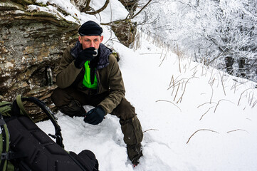 Fototapeta na wymiar A man drinking coffee during a break on a mountain trip in winter.