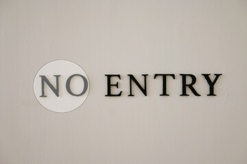 The NO ENTRY sign is installed on the cream-coloured cement wall to inform those involved. The letters NO are circled in white (blurred) and ENTRY in black letters. Black steel letters on ement wall
