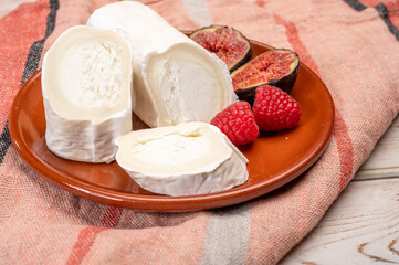 French organic matured white goat cheese with white rind close up served with fresh raspberries and figs
