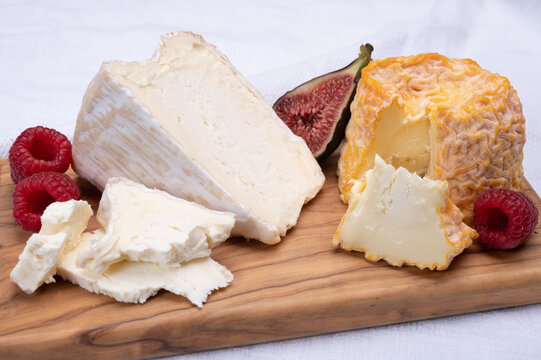 Board with french soft cheeses, Delice de Bourgogne French cow's milk cheese from Burgundy region of France and yellow langres cheese served with fresh raspberries