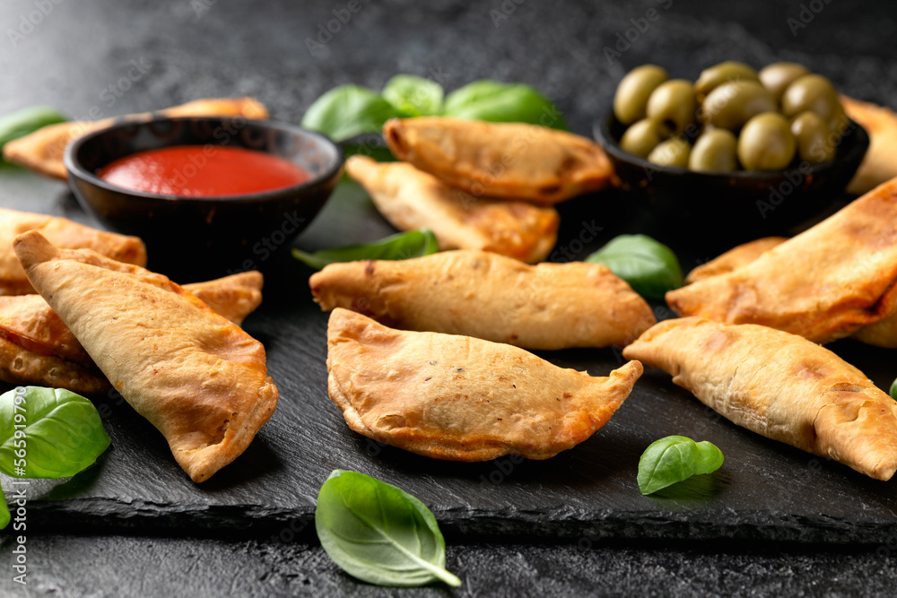 Wall mural Freshly baked mini calzones with bolognese served on black slate board