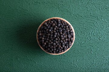 Bowl full of black pepper on a green background