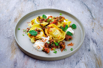 Traditional oriental manti dumplings with spicy minced meat and yogurt served as close up in a nordic design plate with text free space