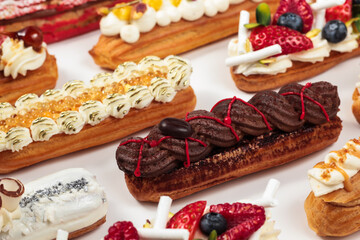 An assortment of éclairs, each topped with intricate details, from delicate chocolate garnish to fresh berries, ready to satisfy any sweet tooth