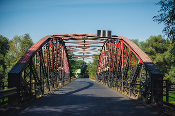 old metal bridge is painted red and black. Steel bridge with asphalt covering in thick vegetation