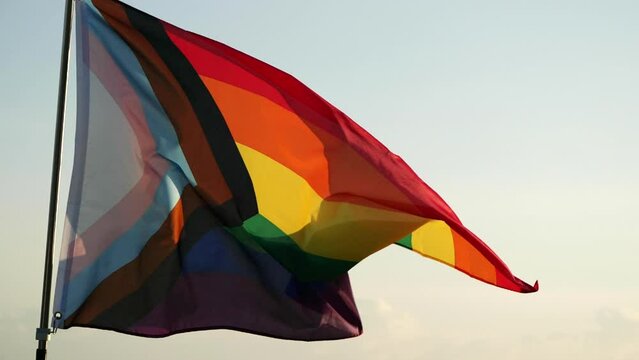 LGBT Pride Flag Waving. New LGBT pride flag is symbol LGBT, Gay, Lesbian, Peace, Pride, LGBTQ, Bisexual, Homosexual, Transgender, Love. Rainbow flag waving on sunset, soft focus. Slow motion