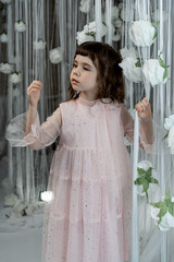 a girl in a pink dress with white roses stands against a white wall