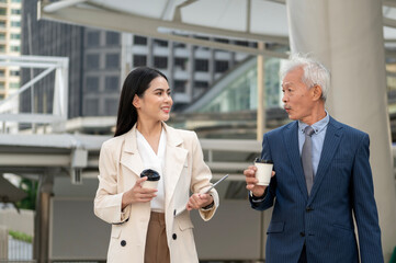 Asian senior mature middle aged businessman and young businesswoman having a discussion and coffee in modern city