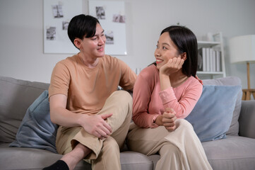 Happy young Asian couple sitting on sofa relaxing together in living room at home
